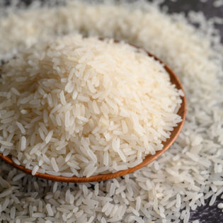 Milled rice in a bowl and a wooden spoon on the black cement floor. Selective focus